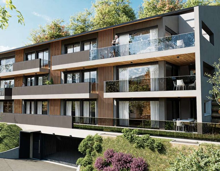 Viale di un moderno edificio residenziale a tre livelli con balconi in vetro, facciate in cemento e dettagli in legno, immerso nel verde.
