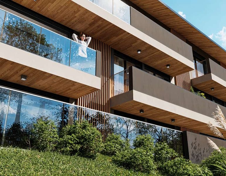 Balcone di un cortile moderno, con vetrate grandi e legno a vista, via a un abitazione contemporanea e giardino curato sottostante.