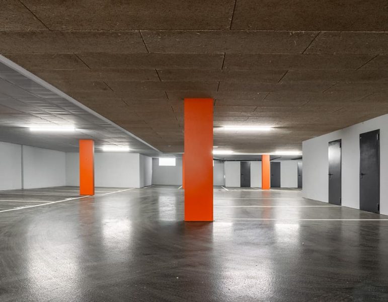 Parcheggio sotterraneo vuoto con colonne arancioni, fondo riflettente e soffitto in cemento.
