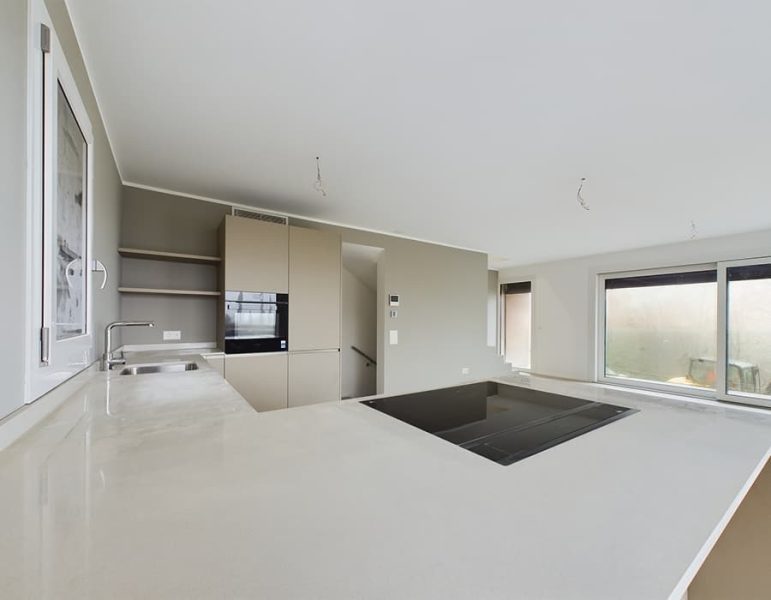 Cucina moderna luminosa con isola bianca e piano nero, armadi coordinati e ampie finestre luminose.